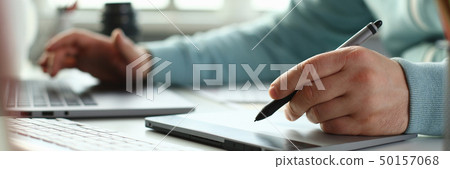 A young designer holds a pen from a tablet in his A young designer holds a pen from a tablet in his 50157068
