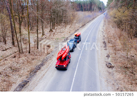 Several cars with kayaks on roof rack driving on the road among trees Several cars with kayaks on roof rack driving on the road among trees 50157265