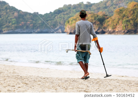 Asian male uses metal detector to find objects on 50163452