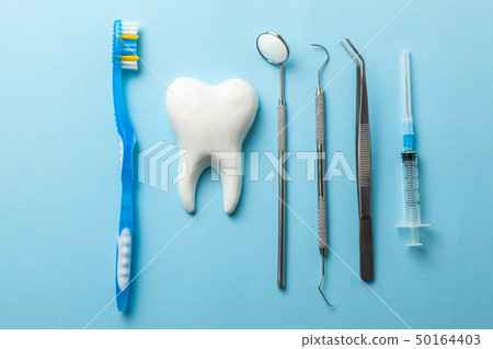 Tooth and dental instruments on blue background. Dental treatment. Dentist tools mirror, hook, 50164403