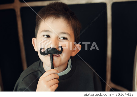 Happy kid posing with a fake moustache on black background Happy kid posing with a fake moustache on black background 50164432
