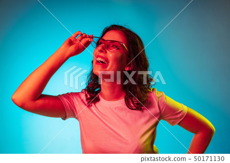 Happy young woman standing and smiling against blue background Happy young woman standing and smiling against blue background 50171130