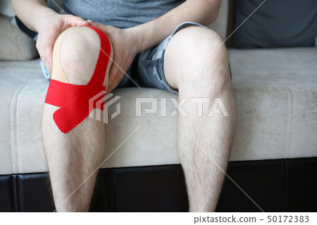 Male hands holding sored knee sitting on couch at home Male hands holding sored knee sitting on couch at home 50172383