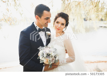 Romantic, fairytale, happy newlywed couple hugging and kissing in a park, trees in background Romantic, fairytale, happy newlywed couple hugging and kissing in a park, trees in background 50173305