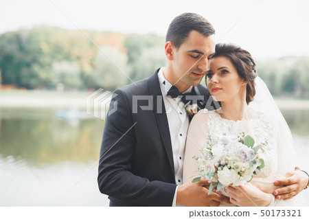 Stylish couple of happy newlyweds walking in the park on their wedding day with bouquet 50173321
