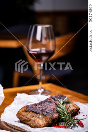 Striploin grilled beef steak served with rosemary, salt and peppercorns on wooden board with glass 50174869