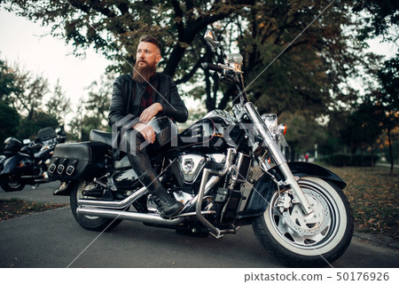 Baerded biker poses on chopper leaning on a helmet 50176926