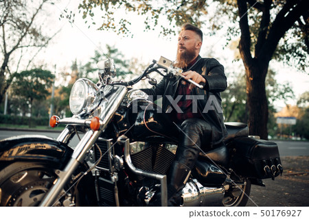 Biker sitting on a motorcycle leaning on a helmet Biker sitting on a motorcycle leaning on a helmet 50176927