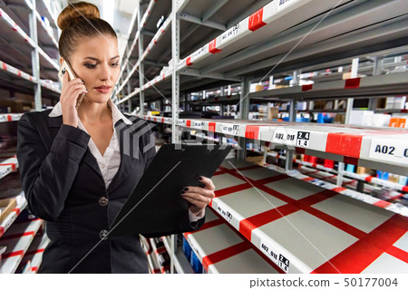 Serious pretty businesswoman talking on phone in hardware shop storage 50177004