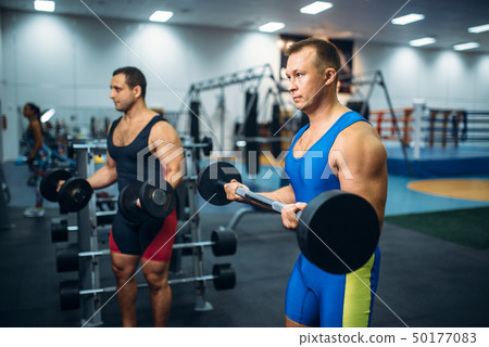 Strong male athletes works with weights in gym 50177083
