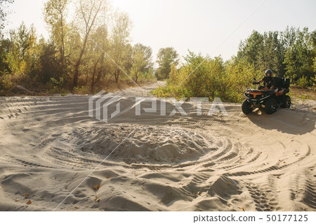 Atv rider in helmet climbing sandy road in forest 50177125