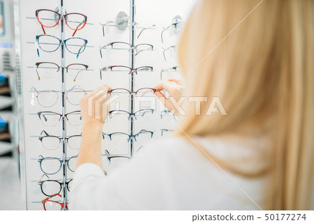 Female optometrist shows glasses in optics store 50177274