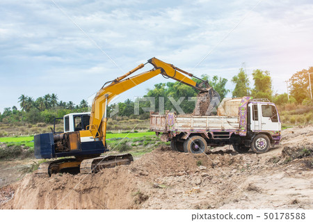 Yellow excavator machine loading soil into a dump 50178588