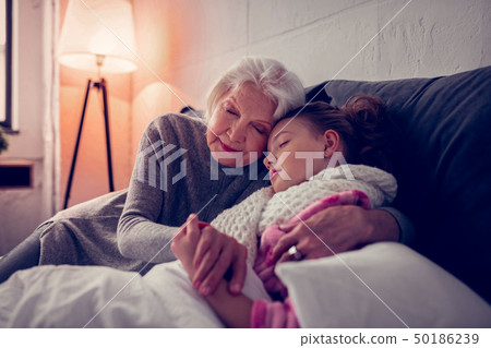 Grey-haired granny hugging her sick cute girl falling asleep 50186239