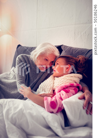 Caring granny hugging her cute girl staying in bed feeling sick 50186246