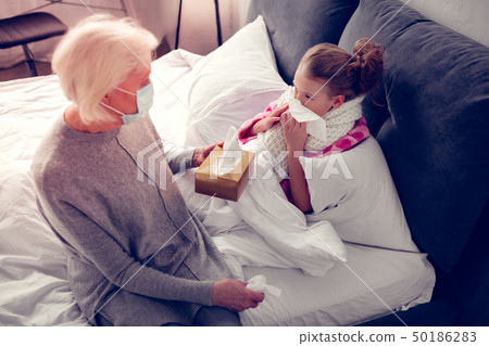 Caring granny giving napkins for her girl having running nose 50186283