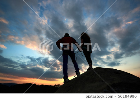 Young woman and man standing on the rock and watching for running clouds. With beautiful sunset on 50194990