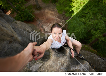 Beautiful young woman climbing on rock outdoors in summer. Top view. Happy girl climbing rock 50195005