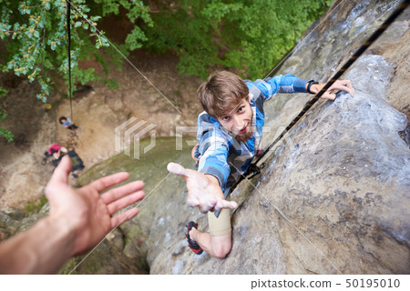 Climber rock climbing overhanging cliff with rope. Asking for help. Man helping his friend to climb Climber rock climbing overhanging cliff with rope. Asking for help. Man helping his friend to climb 50195010