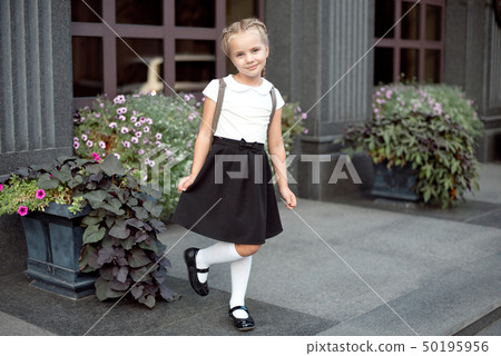 Full-length of a little smiling girl in school uniform posing against a school entrance background 50195956