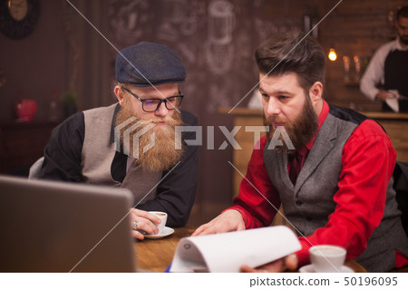 Two bearded collegues working together on a computer in a coffee shop 50196095