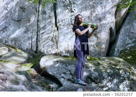 Young attractive girl in the mountains is holding a yoga mat Young attractive girl in the mountains is holding a yoga mat 50201257