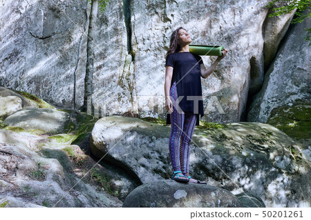 Young attractive girl in the mountains is holding a yoga mat Young attractive girl in the mountains is holding a yoga mat 50201261