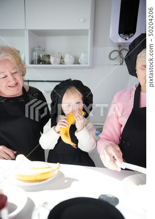 Family standing in the kitchen. A little girl eating banana 50204206