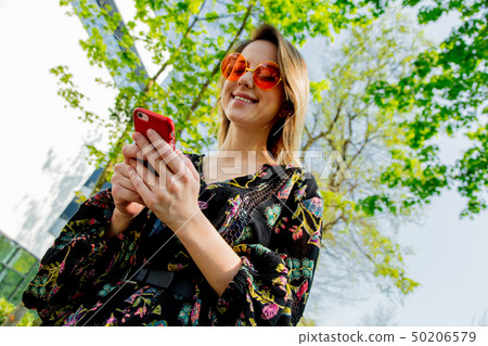 Young woman in sunglasses with mobile phone sitting on green alley near modern building of 50206579