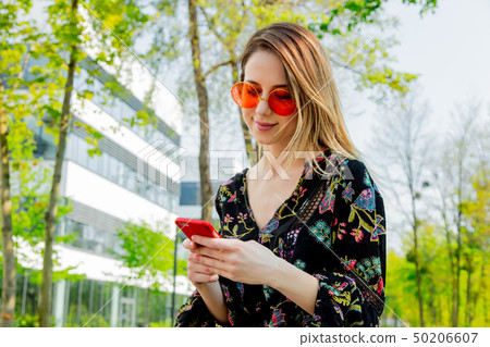 Young woman in sunglasses with mobile phone sitting on green alley near modern building of 50206607