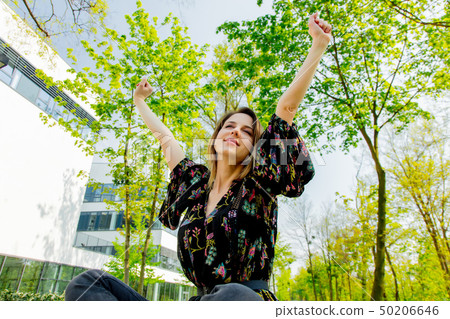 Young girl is stretching while yawning and sitting near modern building of university.  50206646