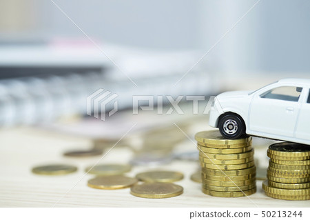 Little white car over a lot of money stacked coins Little white car over a lot of money stacked coins 50213244