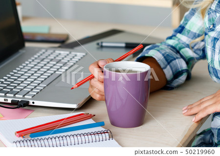 Female designer hands holding cup of hot beverage and drawing with pencil Female designer hands holding cup of hot beverage and drawing with pencil 50219960