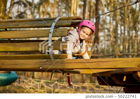 Adorable little girl in helmet in rope park in forest Adorable little girl in helmet in rope park in forest 50222741