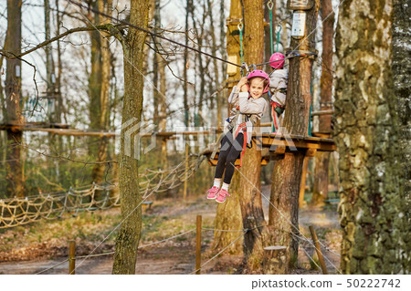 Two adorable little girls in helmet in a rope park in the woods 50222742