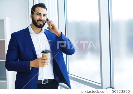 Businessman holding mobile phone and cup of coffee in office buildings in the background. 50223800
