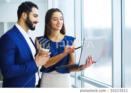 Pretty mixed race woman and her bearded colleague using laptop in order to discuss joint project in 50223811