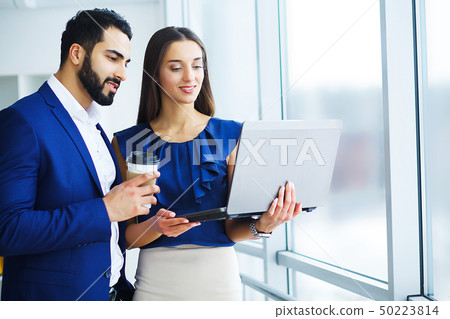 Pretty mixed race woman and her bearded colleague using laptop in order to discuss joint project in 50223814