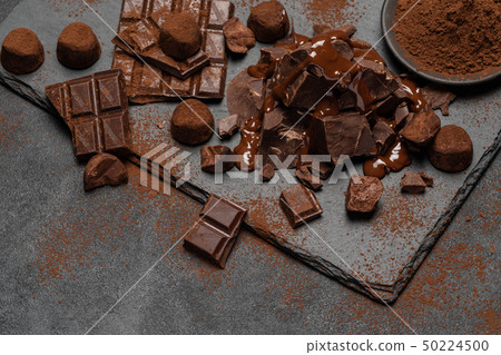 dark or milk chocolate pieces, chocolate syrup and truffle candies on dark concrete background 50224500