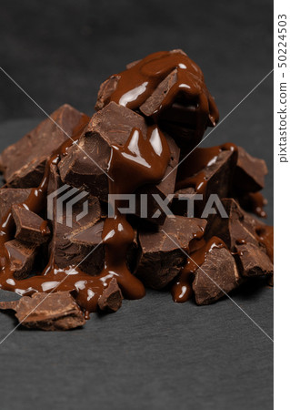 dark or milk chocolate pieces stack and chocolate syrup on dark concrete background 50224503