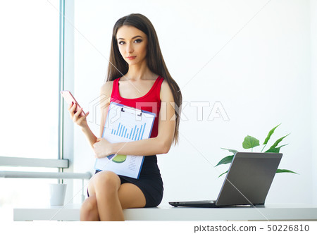 Business. Beautiful Young Woman Works on the Computer. Trims in Hands Phone. Bright Modern Office Business. Beautiful Young Woman Works on the Computer. Trims in Hands Phone. Bright Modern Office 50226810
