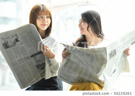 Two women reading a newspaper on the window side Two women reading a newspaper on the window side 50229261