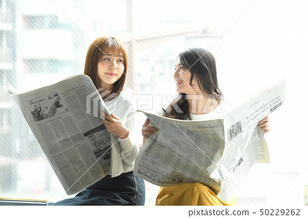 Two women reading a newspaper on the window side Two women reading a newspaper on the window side 50229262