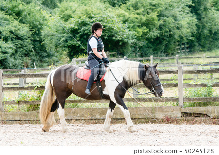 A girl practicing riding on a black and white horse 50245128