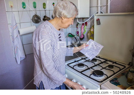 Senior old housewife at home and examines gas and 50248926