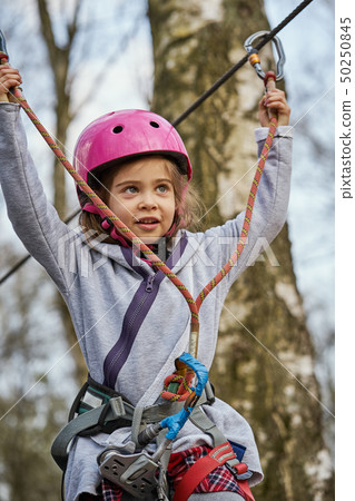 Adorable little girl in helmet in rope park in forest