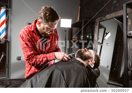 Barber work with clipper machine in barbershop. Professional trimmer tool cuts beard and hair of 50260937