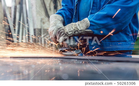 Worker in metal factory grinding workpiece with sparks flying 50263306