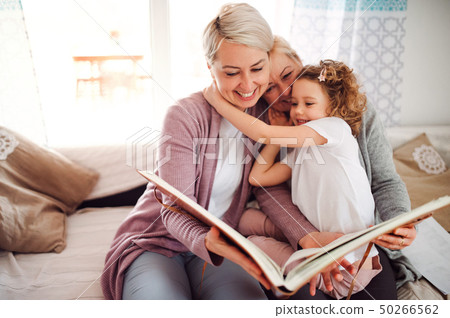 A small girl with mother and grandmother at home, looking at photographs. 50266562