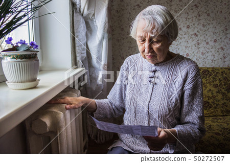 Woman holding cash in front of heating radiator. 50272507